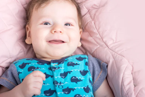Schattige baby in een roze bed. Portret van een baby. Portret van een glimlachend kind. Een kind op een witte bed. Knappe jongen. — Stockfoto