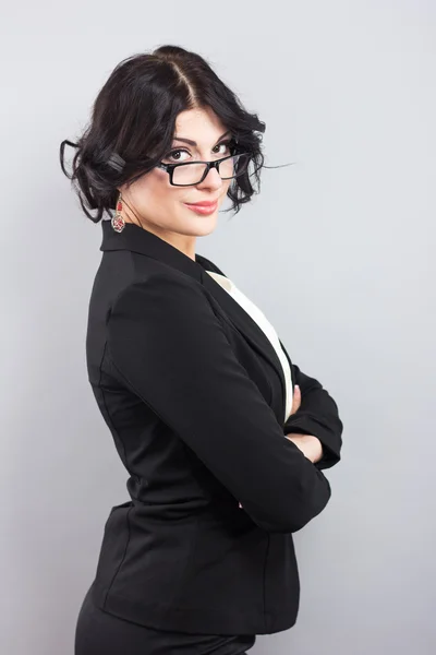 Aantrekkelijke zakenvrouw in een zwarte jas. Mooi meisje met bril in zwart frame. Stijlvolle brunette op een grijze achtergrond — Stockfoto
