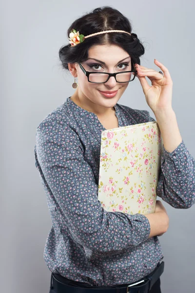 Atractiva estudiante femenina con una carpeta en las manos. Retrato de una hermosa morena sobre un fondo gris. Chica joven con gafas en marco negro —  Fotos de Stock