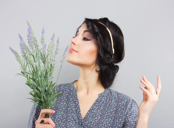 Hermosa morena con una ramita de lavanda. Retrato de una joven sobre un fondo gris. La morena con el corte de pelo griego —  Fotos de Stock