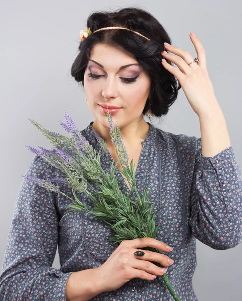 Linda morena com um ramo de lavanda. Retrato de uma jovem em um fundo cinza. A morena com o corte de cabelo grego — Fotografia de Stock