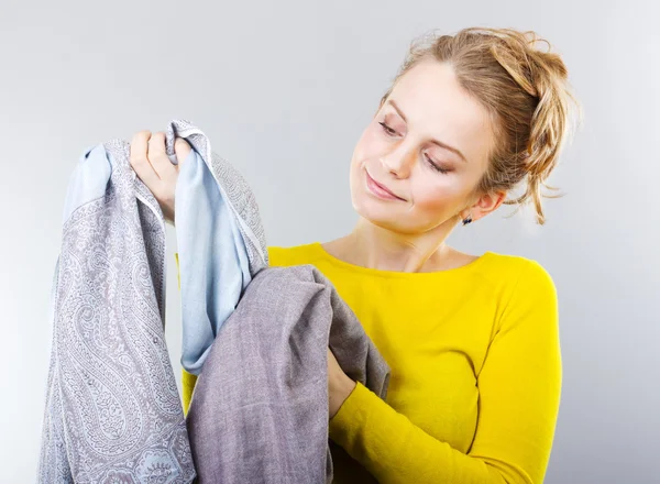 Ellerinde giysileri olan genç bir sarışın. Ev sahibi kıyafetleri nasıl saklayacağını düşünüyor. Kıyafetlerin bakımı, çamaşır deterjanı, giysiler için saç kremi. Alışveriş. — Stok fotoğraf