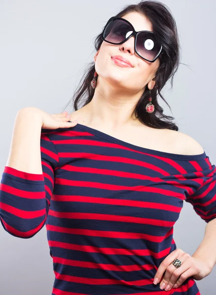 Mooie brunette in een blauwe jurk met rode strepen. Mode. Portret van een jong meisje in zonnebril. — Stockfoto