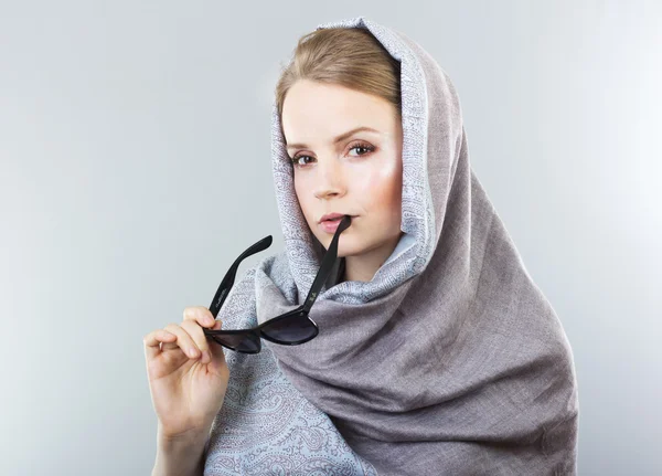 Schöne junge Frau in besticktem Schal und Sonnenbrille auf grauem Hintergrund — Stockfoto