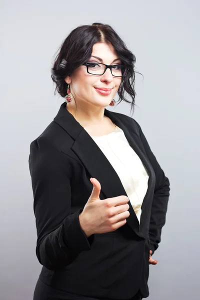 Attractive brunette with glasses showing thumb.Smiling business woman in a strict suit. beautiful business woman in glasses showing thumb up symbol. — Stockfoto