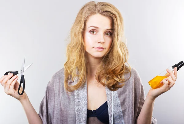 Beautiful curly blonde takes care of her hair.Beautiful woman thinking about hair. Dry hair treatment.Scissors or spray. — Stock Photo, Image