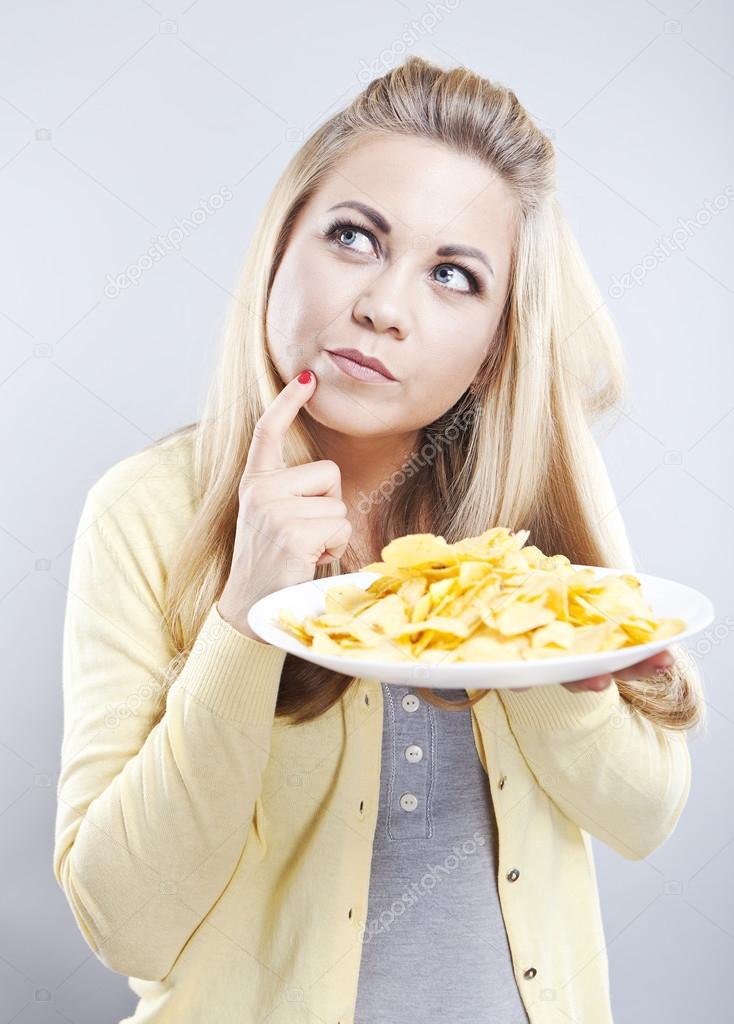 Young girl with potato chips. She thinks. Blonde watch your diet