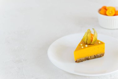 Beyaz tabakta physalis olan bir dilim balkabaklı cheesecake. Yatay yönelim, boşluğu kopyala.