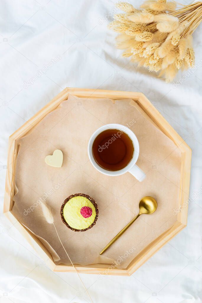 Cake with raspberry and  a cup of tea on a tray and a bouquet of flowers on a white bed. Valentine's day concept. Sugar, lactose, gluten free. Horizontal orientation, top view.