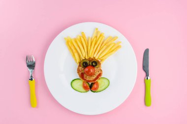 Pembe arka planda çatal ve bıçakla palyaço şeklinde çocuk maması..