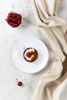 Beyaz tabakta hindistan cevizi kremalı ve kirazlı çiğ kek. Şeker, glüten ve laktozsuz. Dikey yönelim, üst görünüm.