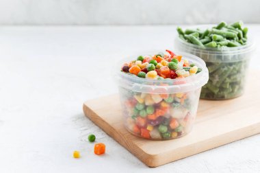 Tahta bir tahtanın üzerindeki konteynırlarda donmuş sebzelerin karışımı. Yatay yönelim, boşluğu kopyala.