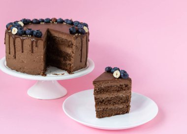 Bir dilim çikolatalı pasta ve pembe arka planda yaban mersini ve fındık..