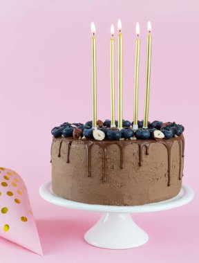 Üzerinde böğürtlen, fındık ve pembe arka planda mumlar olan çikolatalı pasta. Doğum günü konsepti. Şekersiz, glütensiz ve laktozsuz..