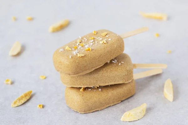 Homemade popsicle with chocolate cashews and mango pieces on a gray background.