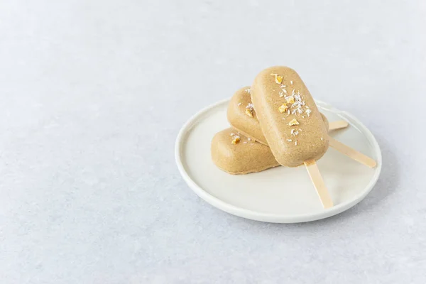 Vegan popsicle with chocolate cashews and mango pieces on a plate. Horizontal orientation, copy space.