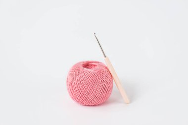 Örgü örmek için pembe iplikler ve beyaz arka planda bir örgü kancası..
