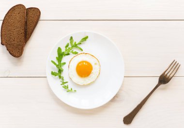 Beyaz tabakta roka ve sahanda yumurta. Yatay yönelim, üst görünüm.