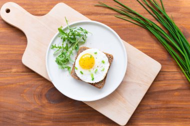 Kızarmış yumurtalı tost, yeşil soğan ve ahşap bir tabakta roka. Yatay yönelim, üst görünüm.