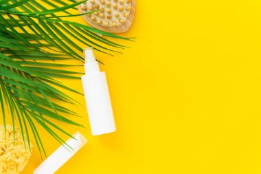 Sarı arka planda palmiye dalları olan kozmetik ürünleri şişeleri. Yatay yönelim, boşluğu kopyala.