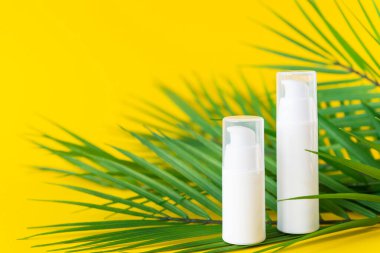 Sarı arka planda palmiye dalları olan kozmetik ürünleri için beyaz plastik kavanozlar..