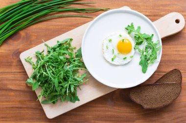 Kahverengi ahşap bir masada roka kaplı sahanda yumurta. Yatay yönelim, üst görünüm.