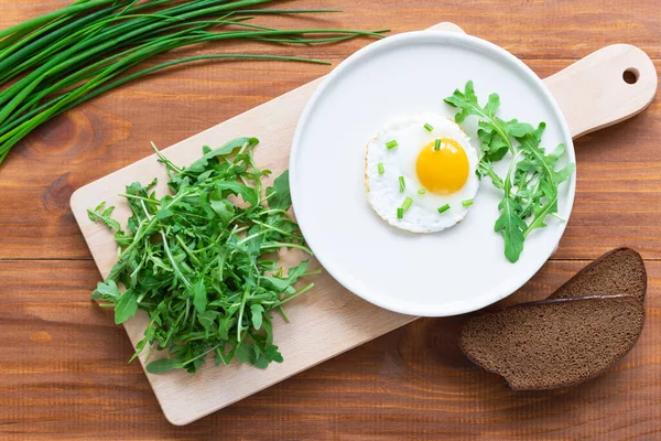 Kahverengi ahşap bir masada roka kaplı sahanda yumurta. Yatay yönelim, üst görünüm.