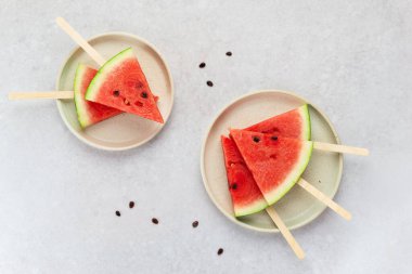 Gri bir masanın üzerinde tabakta tatlı kırmızı karpuz dilimleri. Yatay yönelim, üst görünüm. 