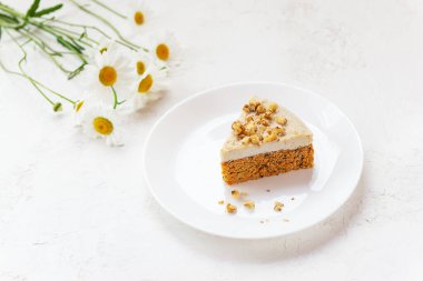 A slice of no baked carrot cake with chamomile flowers on the table.