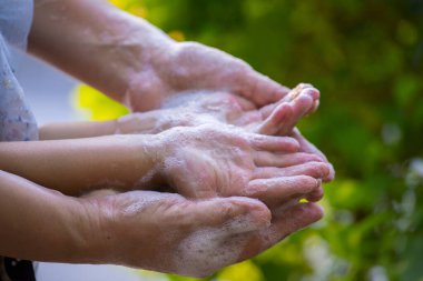 Anne ve çocuk yeşil arka planda sabun ve suyla ellerini yıkıyorlar..