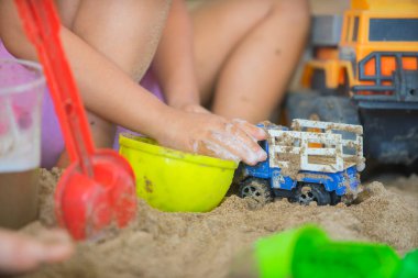 Küçük çocuk kum havuzunda çocuk kamyonuyla oynuyor..