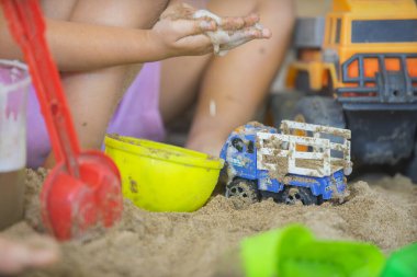 Küçük çocuk kum havuzunda çocuk kamyonuyla oynuyor..