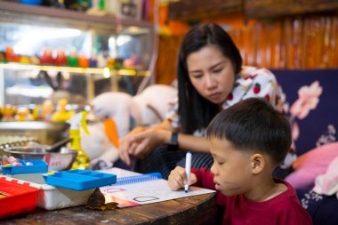 Evde okul kitapları, gazete ve dijital bloknotlarla ev ödevi yapan genç bir öğrenci. Annesi, oğluna ders verirken deftere yazı yazmış. Eğitim, aile hayatı, evde eğitim kavramı