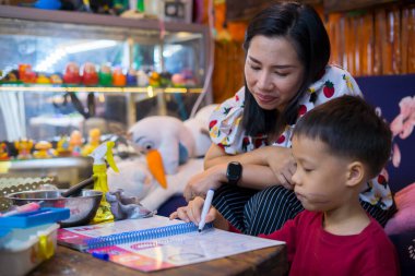 Evde okul kitapları, gazete ve dijital bloknotlarla ev ödevi yapan genç bir öğrenci. Annesi, oğluna ders verirken deftere yazı yazmış. Eğitim, aile hayatı, evde eğitim kavramı