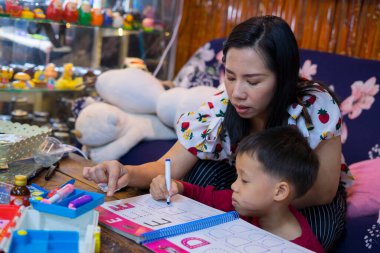 Evde okul kitapları, gazete ve dijital bloknotlarla ev ödevi yapan genç bir öğrenci. Annesi, oğluna ders verirken deftere yazı yazmış. Eğitim, aile hayatı, evde eğitim kavramı