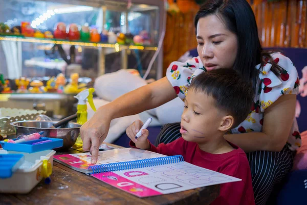 Evde okul kitapları, gazete ve dijital bloknotlarla ev ödevi yapan genç bir öğrenci. Annesi, oğluna ders verirken deftere yazı yazmış. Eğitim, aile hayatı, evde eğitim kavramı