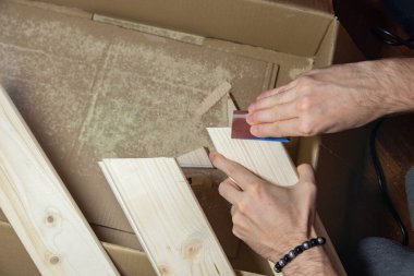 Bir adam evinde zımpara kağıdıyla ahşap bir tahtayı zımparalıyor, DIY