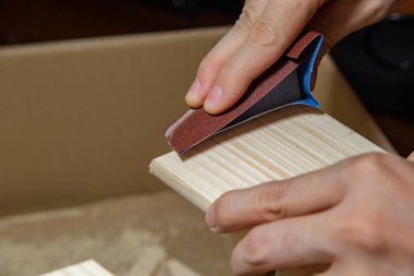 Bir adam evinde zımpara kağıdıyla ahşap bir tahtayı zımparalıyor, DIY