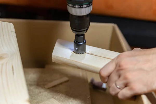 man drills a hole in a wooden board on a box at home handmade