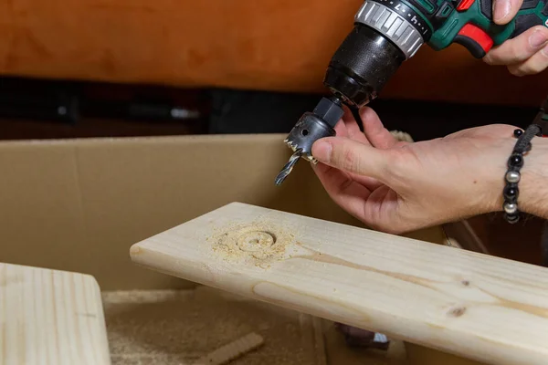 man drills a hole in a wooden board on a box at home handmade