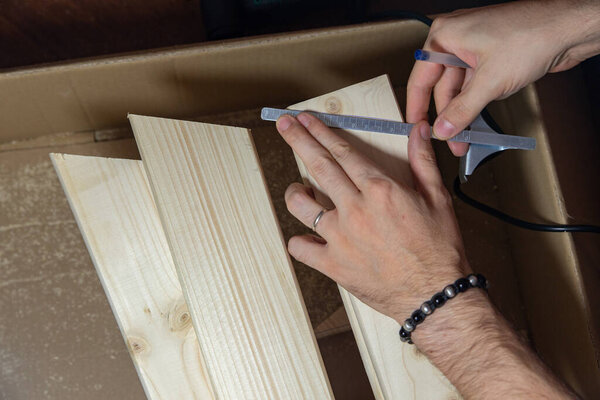 мужчина измеряет линии на деревянной доске на картонной коробке домашней ручной работы