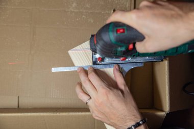 Adam evdeki elektrikli yapbozu karton bir kutunun tahta parçasını kesmek için kullanıyor. Kendin yap..