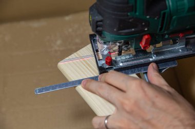 Adam evdeki elektrikli yapbozu karton bir kutunun tahta parçasını kesmek için kullanıyor. Kendin yap..