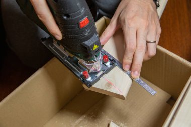 Adam evdeki elektrikli yapbozu karton bir kutunun tahta parçasını kesmek için kullanıyor. Kendin yap..