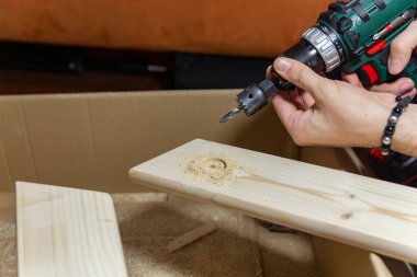 Evde elektrikli matkap kullanarak tahta bir tahtaya delik açan bir adam. Kendin yap..