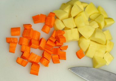 Soyulmuş patates ve havuç beyaz bir tahtada kesilmiş.