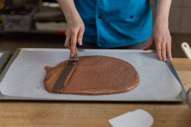 Çikolata hamurunu pasta kağıdına spatula ile yayar.