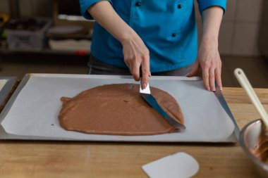 Çikolata hamurunu pasta kağıdına spatula ile yayar.