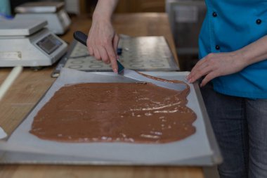 Çikolata hamurunu pasta kağıdına spatula ile yayar.
