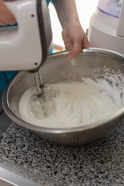 Kadın proteinleri metal bir kasede karıştırıcıyla dövüyor.